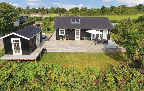 Une maison à deux étages avec une terrasse, un petit abri de jardin et un jardin.