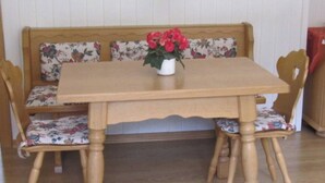 A wooden table with a floral cushion bench, a white vase with flowers, and wooden chairs.
