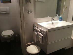 A bathroom with a toilet, sink, mirror, and a small stool.