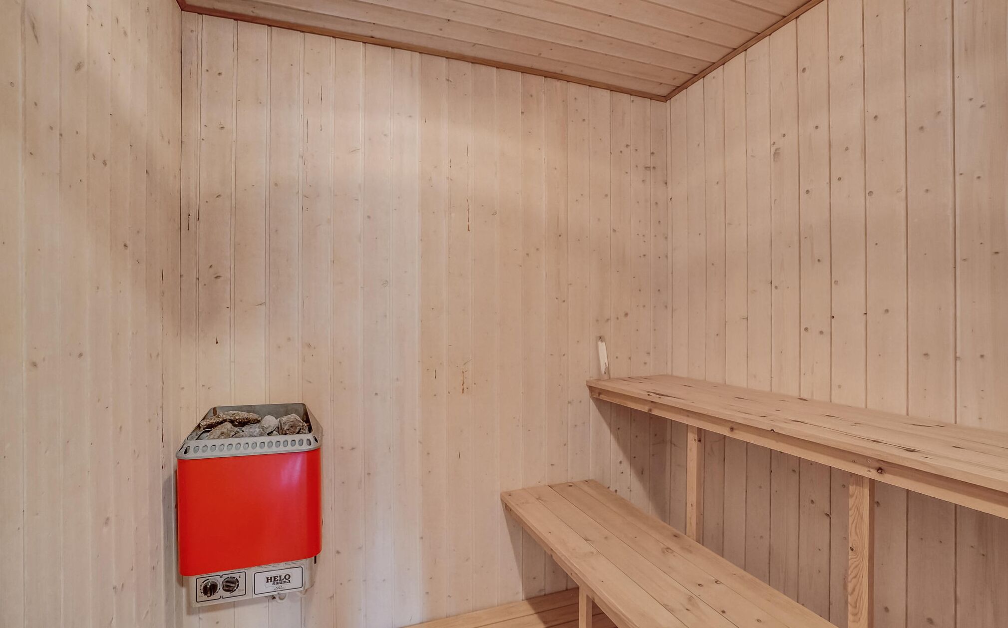 Una sala de sauna con paredes de madera, un banco y un calentador de sauna rojo.