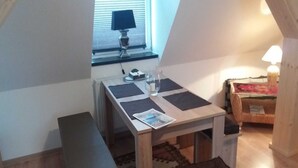 A small, cozy room with a wooden table, a bench, and a window with blinds. - Apartment 3 - Guesthouse Alte Schule (Schwarz)