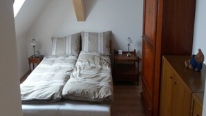A bedroom with a bed, two bedside tables with lamps, a wooden wardrobe, and a small figurine on top. - Apartment 3 - Guesthouse Alte Schule (Schwarz)