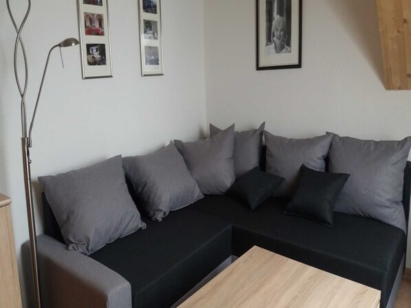 Uma sala de estar moderna com um sofá preto, almofadas cinzas, uma mesa de centro de madeira e um abajur.