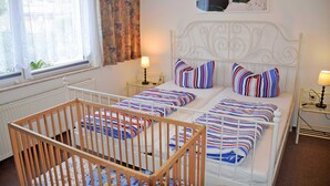 A room with two beds, a crib, and a window with curtains. - Ferienappartement 05 - Pension in Ostseebad Sellin (Sellin)