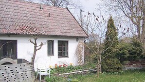 Una casa bianca con tetto in tegole rosse, un piccolo giardino fiorito e una recinzione in legno.