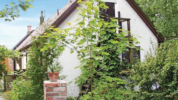 Una casa bianca con tetto spiovente, immersa nel verde e con un comignolo in mattoni.