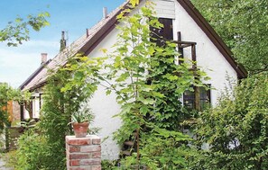 Een wit huis met een steil dak, omringd door weelderige begroeiing en een bakstenen schoorsteen.