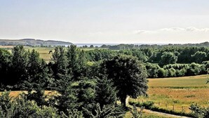 A rural landscape with fields, trees, and a distant body of water under a clear sky.
