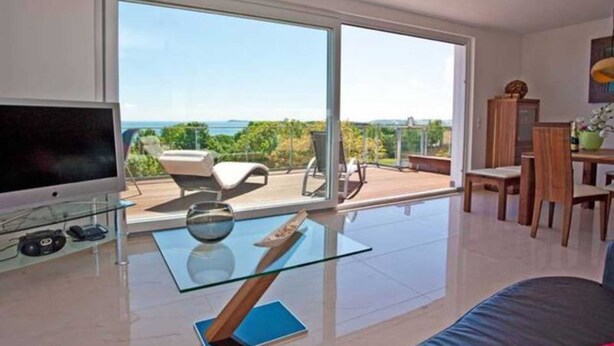 A modern living room with a large TV, glass coffee table, and a view of the outdoors.