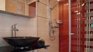A modern bathroom with a glass-enclosed shower, a black sink, and a red accent wall.
