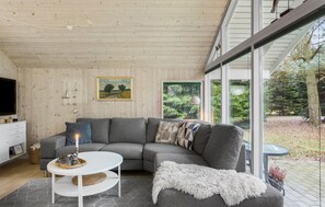 Relax in this stylish living room with a large sofa, coffee table, and side table, featuring a TV and a beautiful garden view.