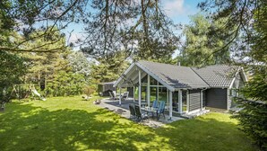 Een gezellig chalet met terras, omgeven door weelderige begroeiing en bomen.