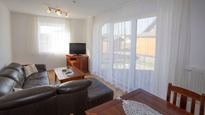 A living room with a leather sofa, a wooden coffee table, a television, and large windows with sheer curtains. - Whg 3 - ground floor villa Boddenblick (Wiek)