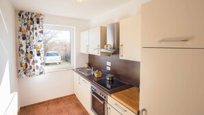 A compact kitchen with a window, a stove, and a refrigerator. - Whg 3 - ground floor villa Boddenblick (Wiek)