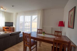 Un coin repas avec une table en bois, quatre chaises, une lampe rouge et un téléviseur posé sur un meuble en bois.