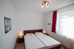 Une chambre à coucher avec un lit, deux tables de chevet avec des lampes, un rideau rouge et une fenêtre ornée de rideaux blancs et légers.