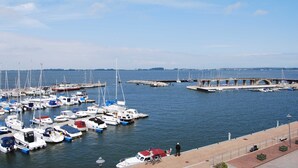 A marina with numerous boats docked, a pedestrian walkway, and a bridge in the background. - Whg 3 - ground floor villa Boddenblick (Wiek)