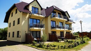 A two-story residential building with balconies, a paved driveway, and a small garden area. - Whg 3 - ground floor villa Boddenblick (Wiek)