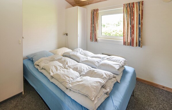 A single bed with a blue mattress and white bedding in a room with white walls, a window with striped curtains, and a wooden ceiling. - Amazing home in Egernsund with sauna (Egernsund)