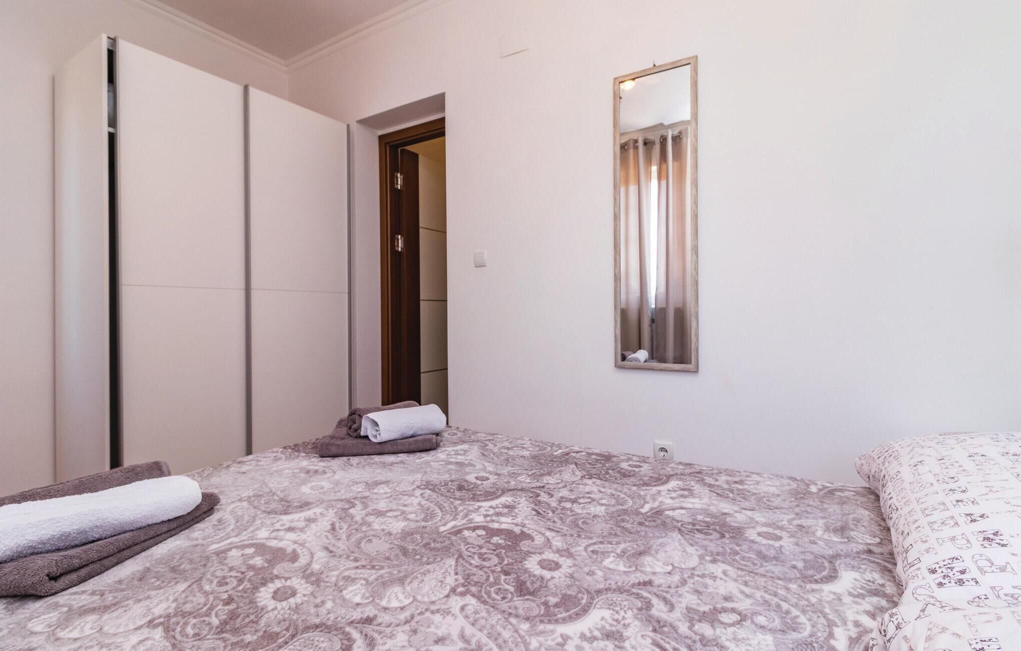Un dormitorio con cama, armario, espejo y puerta que da a otra habitación.
