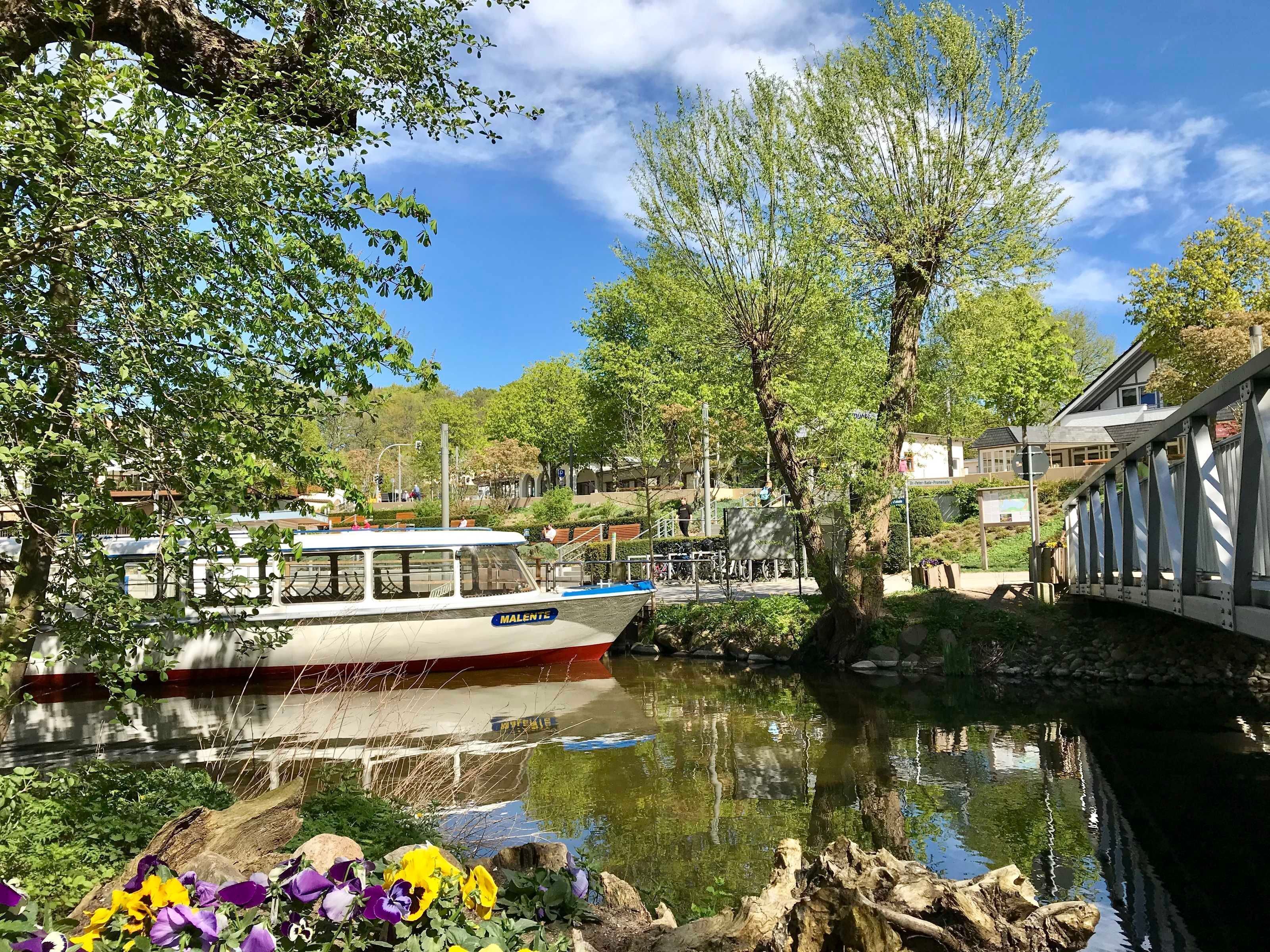 A river with a boat docked, surrounded by greenery and buildings.