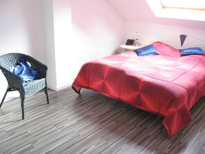 Une chambre à coucher avec un lit, une chaise, une table de chevet et une fenêtre.
