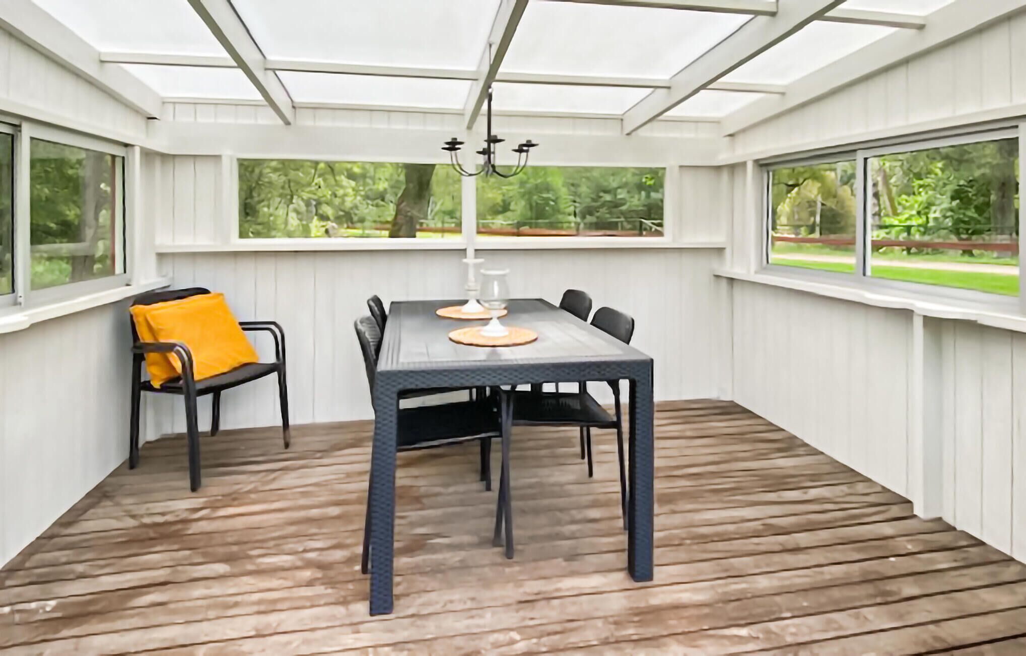 Une véranda avec une table et des chaises, de grandes fenêtres et une vue sur la verdure.