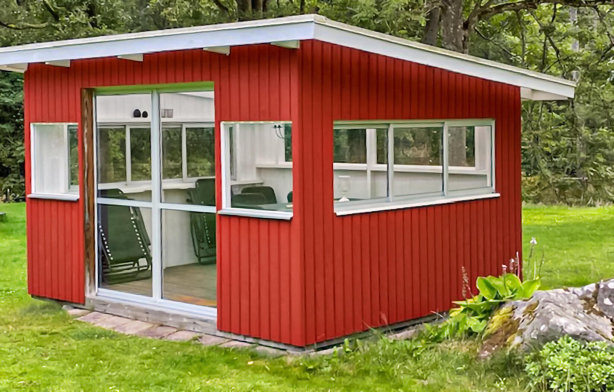 Punainen puinen rakennelma, jossa on lasiovi ja -ikkunat, todennäköisesti pieni mökki tai varasto.