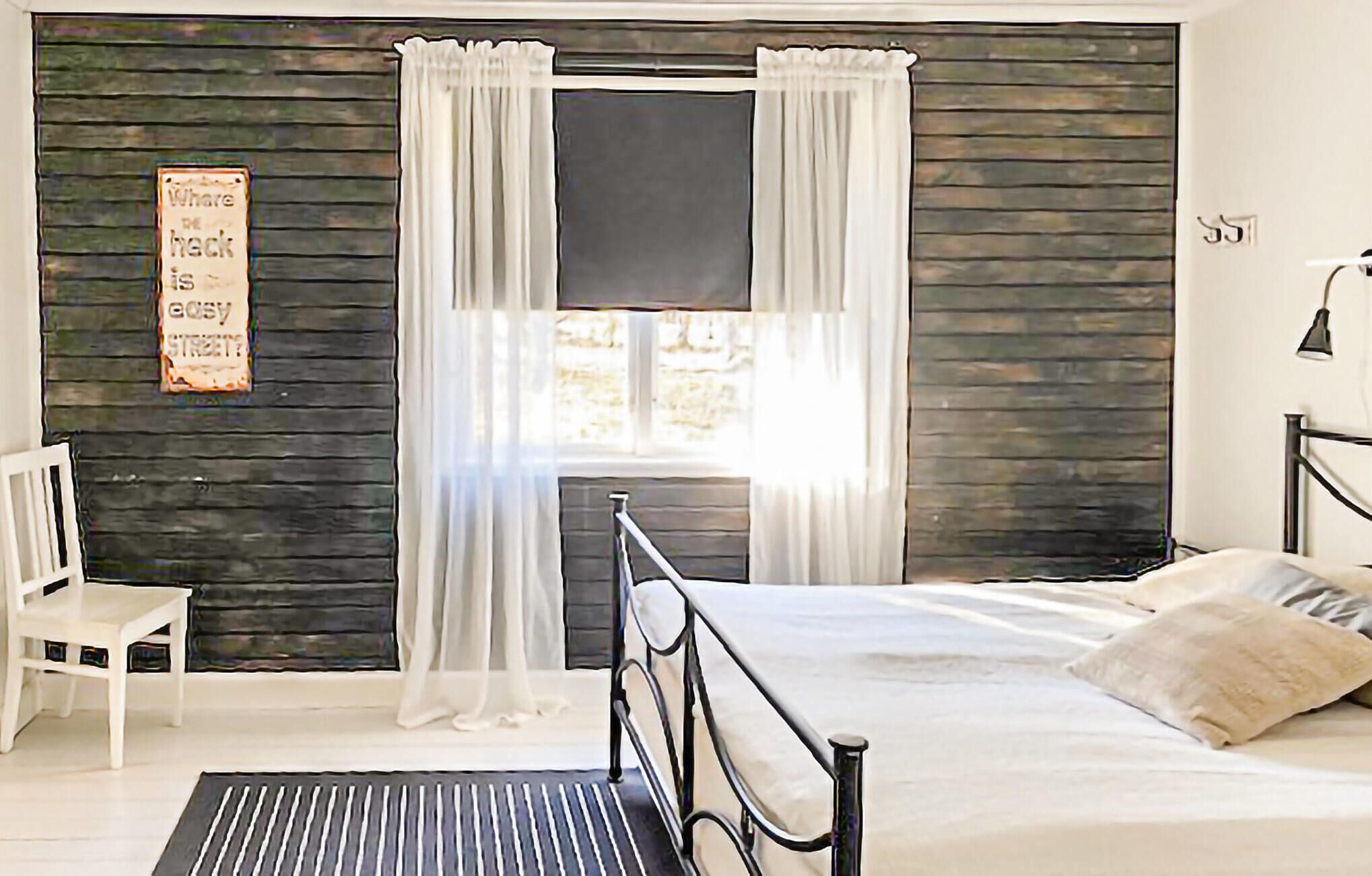Une chambre à coucher avec un lit, une chaise, une fenêtre avec des rideaux et un panneau accroché au mur.