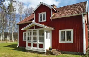Une maison rouge à deux étages, avec un toit à pignon, des boiseries blanches et un porche à l’avant.