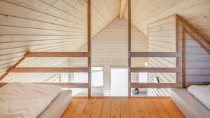 Ein Schlafzimmer im Dachgeschoss mit hohen Decken, Holzbalken, zwei Betten und Blick ins Freie.