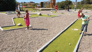Ein Minigolfplatz mit Puttinggrün, einem Sandbunker und einer Holzkonstruktion im Hintergrund.