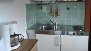 Eine kleine Küche mit Mikrowelle, Herd und Kaffeemaschine. Es gibt Schränke und eine geflieste Spritzschutzwand.