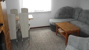 Ein Wohnzimmer mit grauem Sofa, einem Holztisch und einem Essbereich mit weißen Stühlen und einem kleinen Tisch.