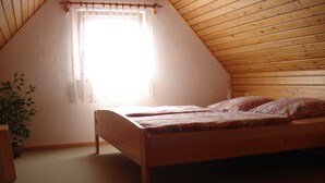 Ein Einzelbett aus Holz in einem Raum mit schrägem Dach und einem Fenster mit Vorhang.