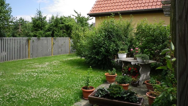 Ein Wohngrundstück mit einem Haus mit roten Ziegeldach, einem Holzzaun und verschiedenen Topfpflanzen.