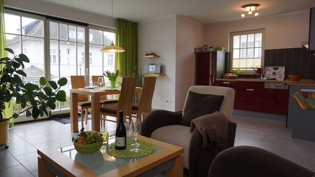 A modern kitchen with a built-in oven, a dining area with a table set for two, and a large window with curtains.