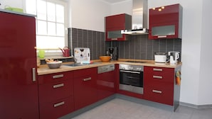 A modern kitchen with red cabinets, a dishwasher, a stove, and a toaster.