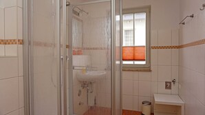 A bathroom with a glass shower enclosure, a sink, and a window with blinds.