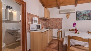 Eine kompakte Küche mit Mikrowelle, Kaffeemaschine und kleinem Spülbecken. Ein Essbereich mit Tisch und Stühlen sowie ein Blumengemälde an der Wand.