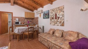 Ein gemütlicher Raum mit Holzbalkendecke, Steinwand, einer Couch und einem Essbereich mit Tisch und Stühlen.