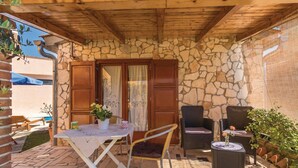 Eine Steinterrasse mit Tisch und Stühlen, ein kleiner Tisch mit Blumenvase und eine hölzerne Pergola darüber.