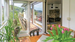 A balcony with a view of a green landscape, a wooden table with a vase of pink tulips, and a glass door leading to an interior space with a stone wall and a chair. - Stunning apartment in Hinterweidenthal (Hinterweidenthal)