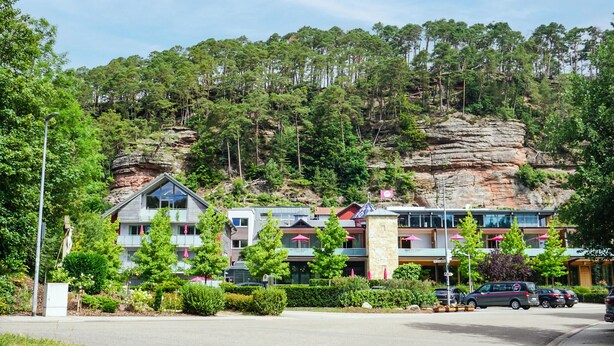 A hotel with multiple floors, a rocky hill in the background, and a parking area with cars. - Stunning apartment in Hinterweidenthal (Hinterweidenthal)