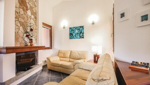 Ein Wohnzimmer mit Kamin aus Stein, einem beigen Sofa, einem Couchtisch und einem Gemälde an der Wand.