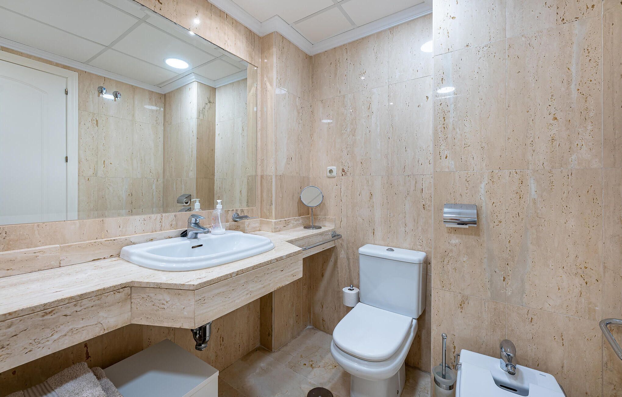 A bathroom with a marble sink, a toilet, and a mirror.