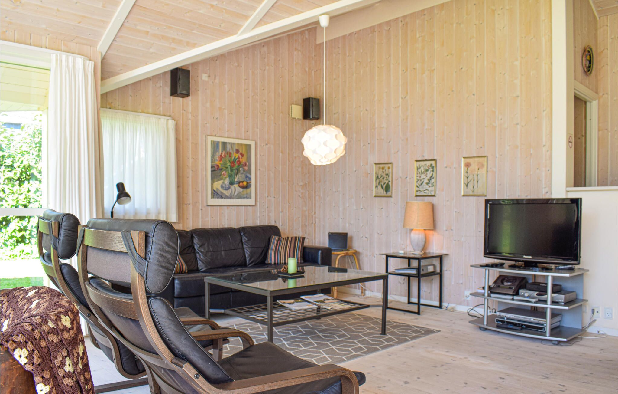 A living room with a leather sofa, a glass coffee table, a TV on a stand, and wooden panel walls.
