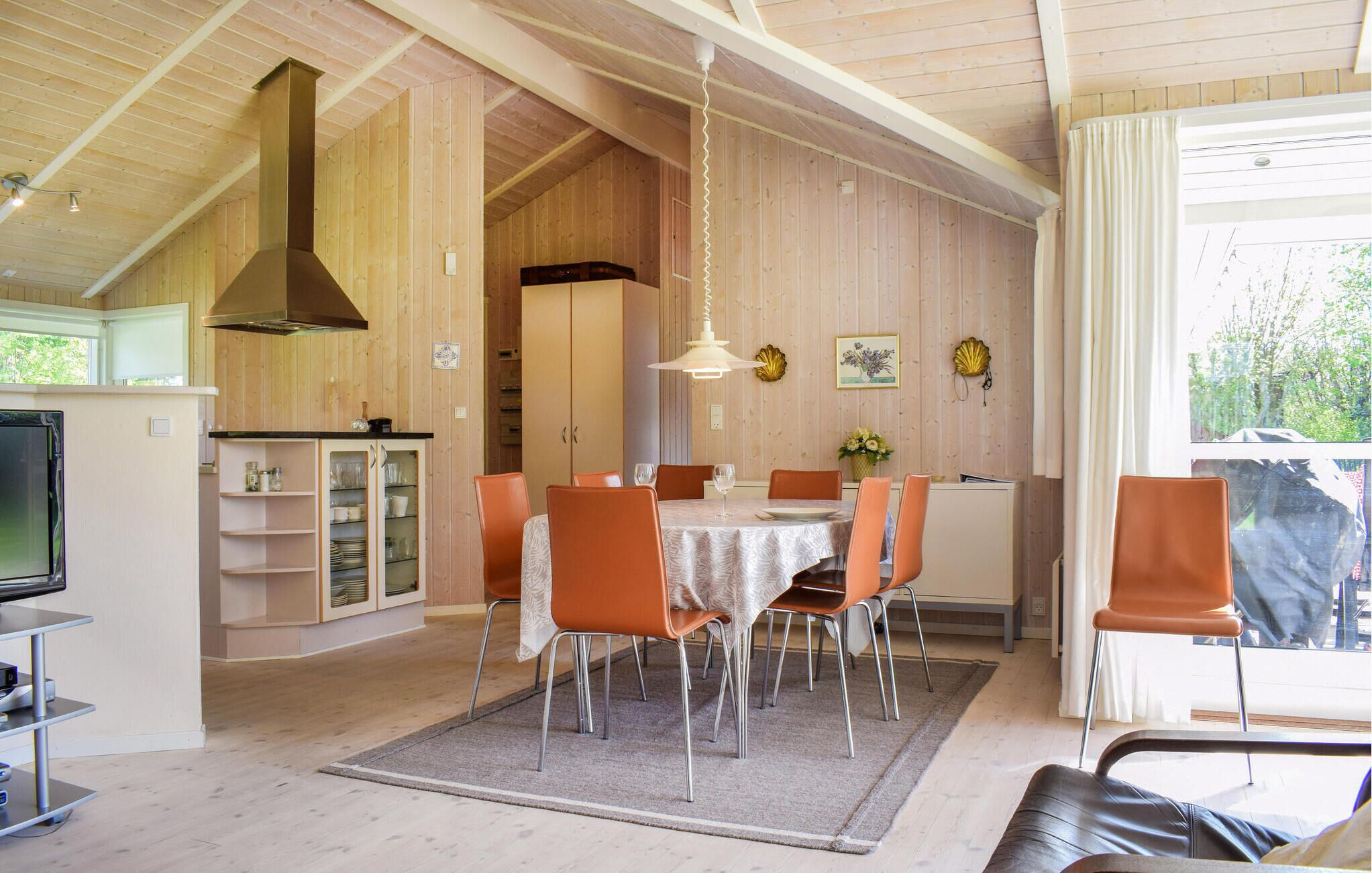 Een eetgedeelte met een tafel voor vier personen, omringd door oranje stoelen, een kroonluchter en uitzicht op groen buiten.