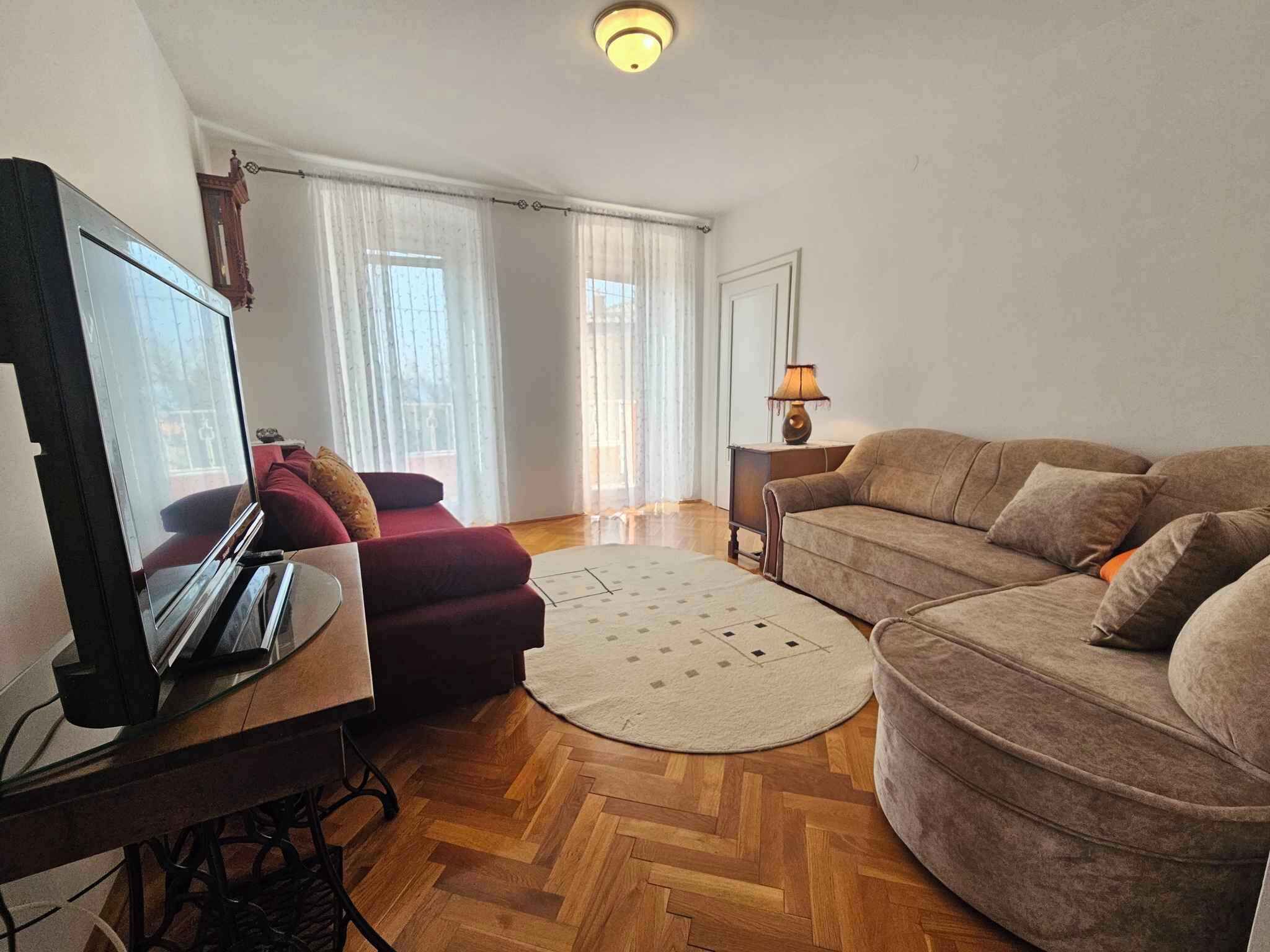 Ein Wohnzimmer mit einer Couch, einem roten Sessel, einem Fernseher und einer Lampe.