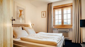 A hotel room with a bed, a window with curtains, a radiator, and a framed picture on the wall. - Basic double rooms (16m²) - Hotel & Restaurant Alpenrose Bayrischzell (Bayrischzell)
